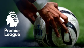 imagem apenas das mãos de um jogador ajeitando a bola para cobrar uma falta ou pênalti, com a logo da Premier League à esquerda na imagem